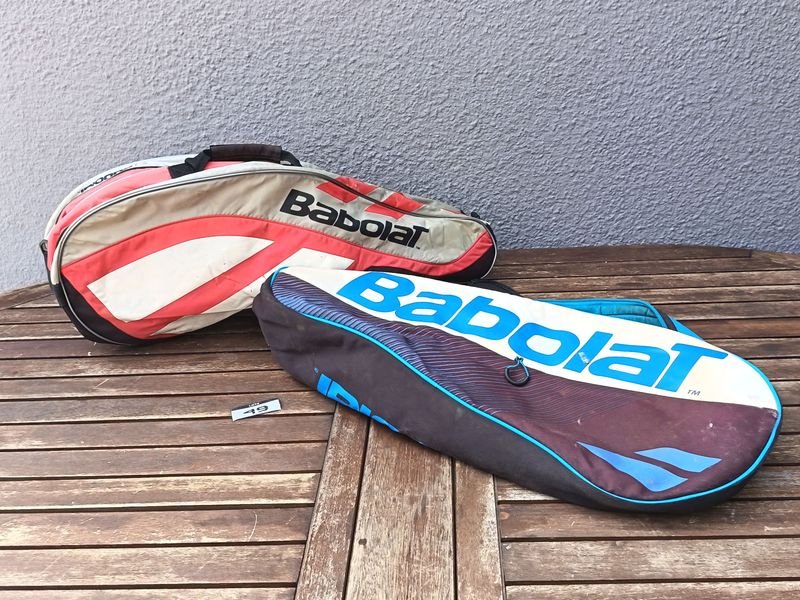 Dos bolsos o fundas para raquetas de tenis marca Babolat, de diferentes modelos y colores, con cierres; usados, con desgaste y señales de uso visibles.