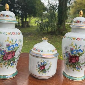 Lote siguiente: 1 juego en porcelana española V.P compuesto por 2 jarrones tipo potiche y 1 alajero con tapa. Su diseño es fino y elegante con montivos florales y guardas al rededor de las piezas montadas sobre un platillo (24 y 13 las medidas)