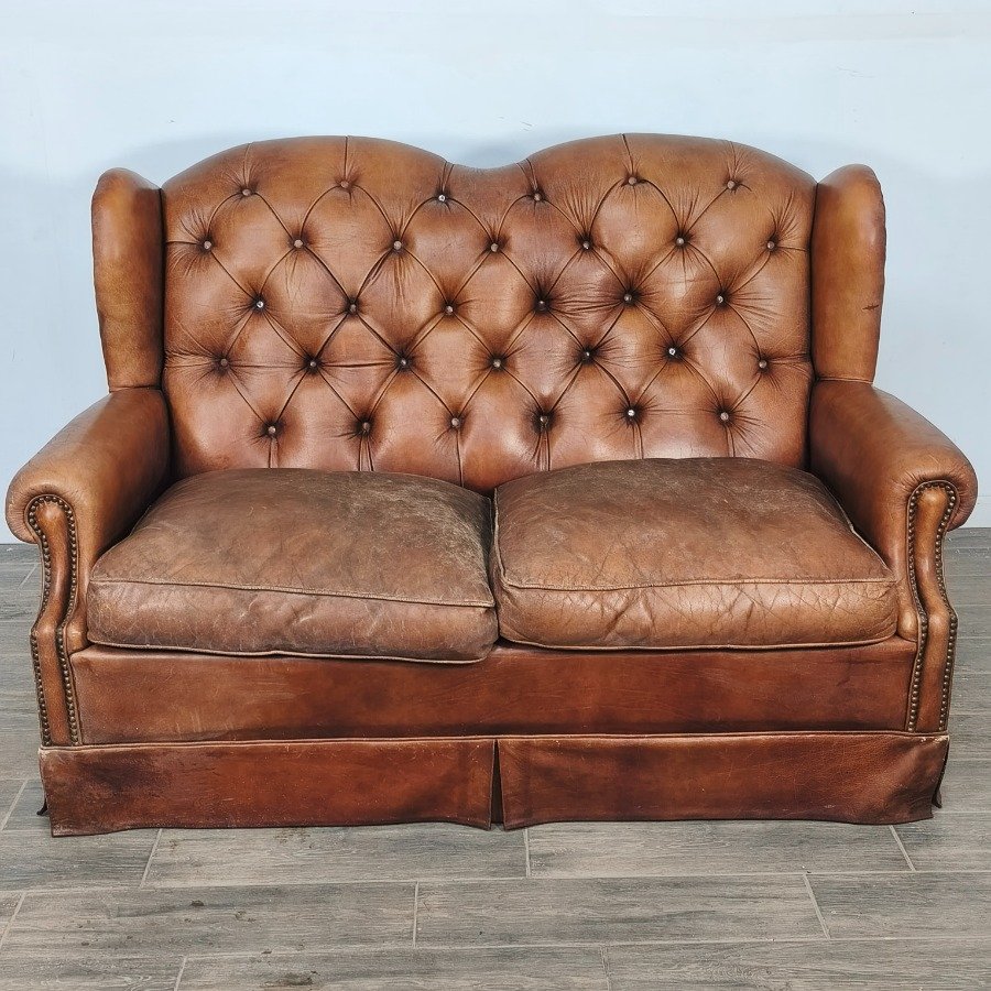 Lote siguiente: Sillón de cuero natural con respaldo capitoneado y almohadones desgastados