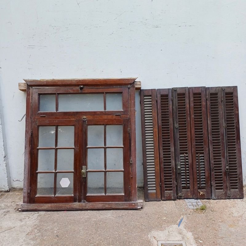 Lote siguiente: Ventana con dos hojas batientes, banderola superior y postigos en cedro con marco de pinotea