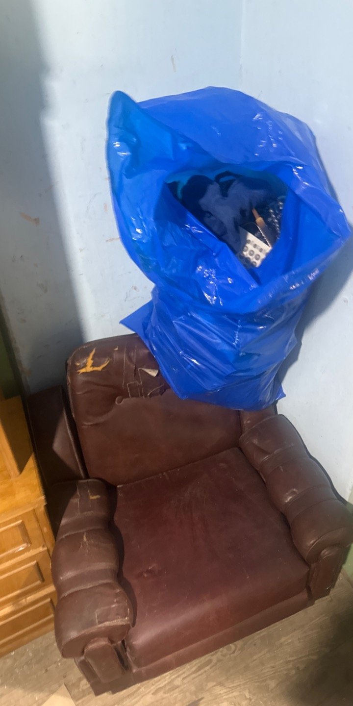 Sillón de cuero marrón con bolsa de perchas y ropa