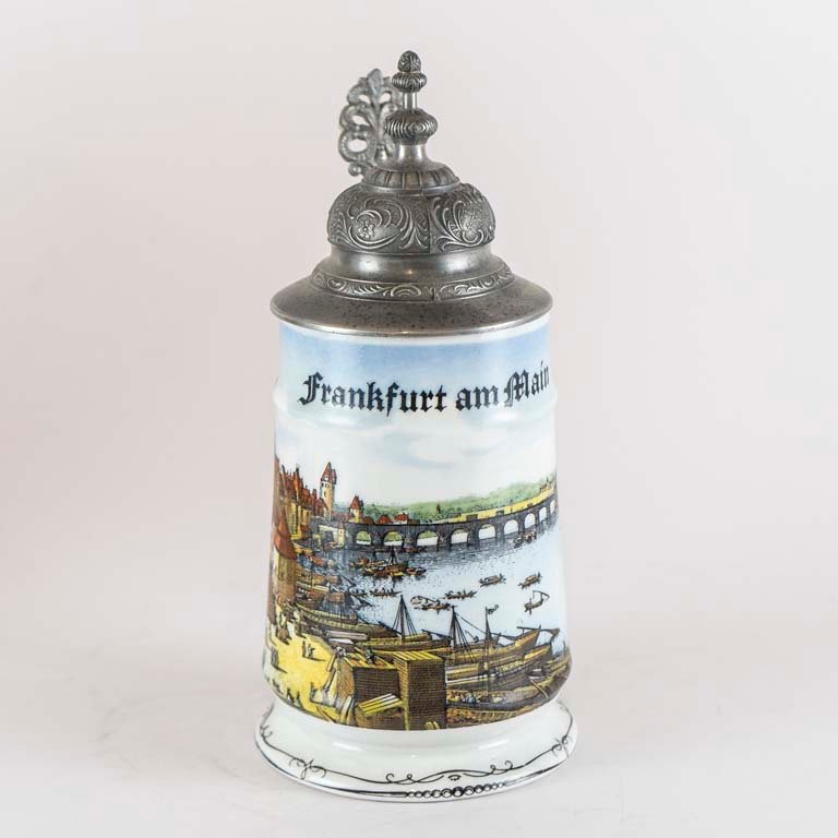 Lote siguiente: Jarra de cerveza de porcelana con tapa de metal y diseño decorativo
