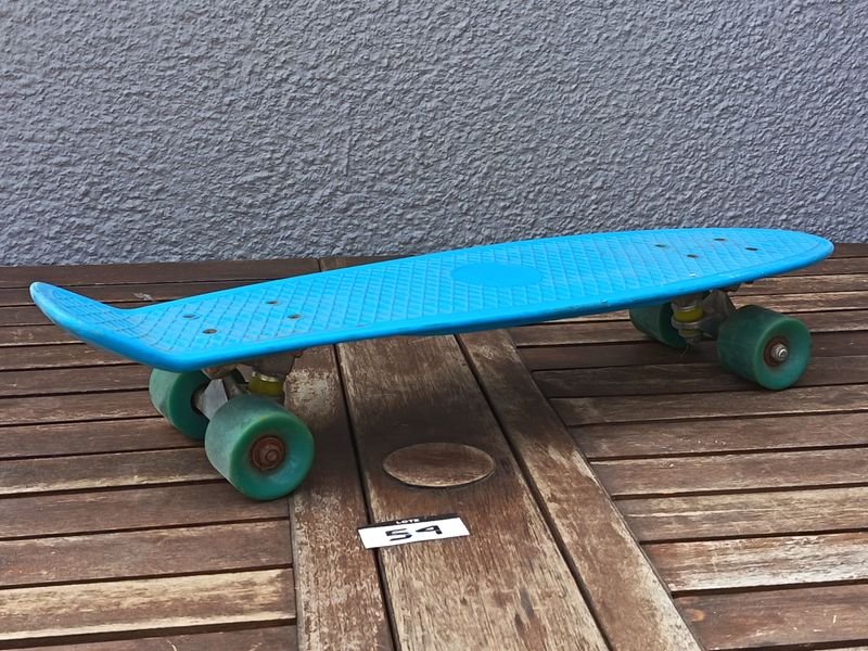Skate tipo cruiser de plástico color celeste, con cuatro ruedas y ejes metálicos; usado.