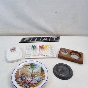 Lote siguiente: L 412 - 7 Piezas - Lote surtido con insignia de auto Fiat, dos ceniceros, un abridor de botellas en madera, y tres piezas de loza decorada con