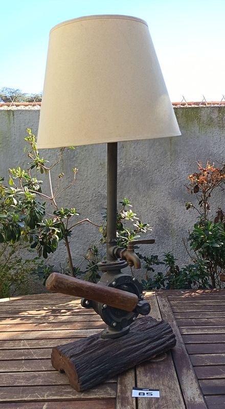 Lámpara de mesa artesanal de estilo rústico La base está compuesta por un robusto medio tronco de madera noble con su corteza natural texturizada, sobre el cual se monta el cuerpo principal de una antigua bomba de agua manual giratorio de hierro fundido No. 2 Allwilen Original Pumpe. Incorpora detalles de fontanería vintage como cañerías de hierro y una canilla de bronce decorativo en el eje. En Muy bueno estado de Conservación. Medidas Sin pantalla: Alto 72 cm - Base Largo 33 cm