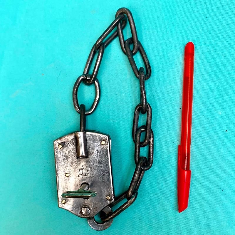 Antiguo candado de estancia con cadena integrada. Con llave. Funcionando. Sellado con el logo de un perro ovejero apoyado en un candado.