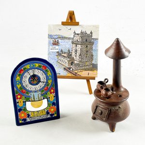 Lote siguiente: Lote de 3 piezas decorativas: Reloj de cerámica, figura de estufa y azulejo con trípode